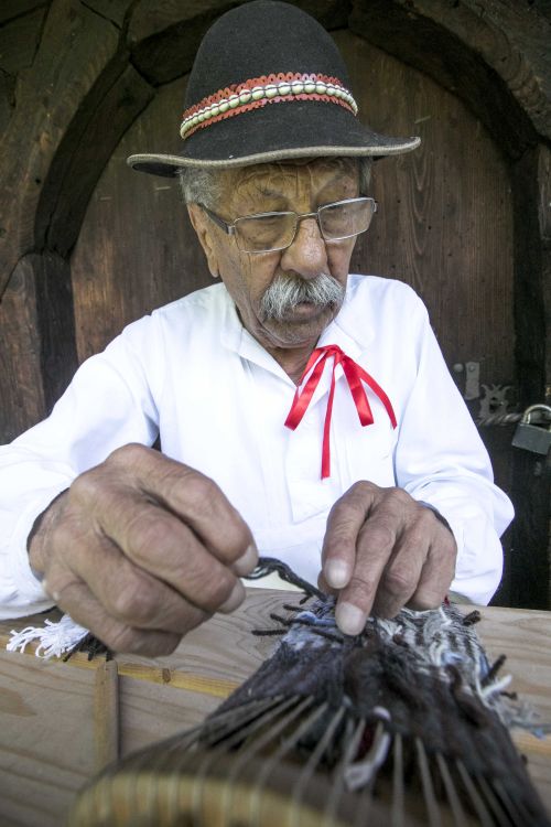 Mężczyzna w kapeluszu góralskim robi rękawice z grubej włóczki