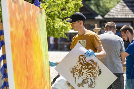 Mężczyzna trzyma obraz tygrysa, przed nim obraz malowany sprayem, za nim ludzie.