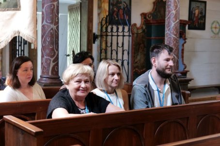 Kilka osób siedzi na ławkach i słucha koncertu w kościele