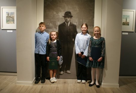 Czwórka dzieci, w tle duże zdjęcie - postać mężczyzny w kapeluszu