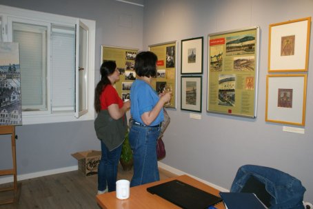 Dwie kobiety, oglądają wystawę, jedna trzyma kieliszek.