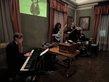 Czterech mężczyzn: jeden gra na pianinie, drugi na gitarze, trzeci na skrzypcach, czwarty na perkusji.
