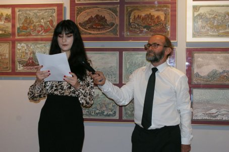 Kobieta mówi i trzyma kartkę, obok mężczyzna trzyma mikrofon, w tle obrazy