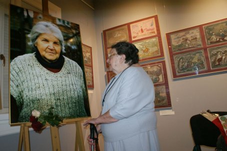 Kobieta patrzy się na fotografię na stelażu, w tle obrazy, krzesło