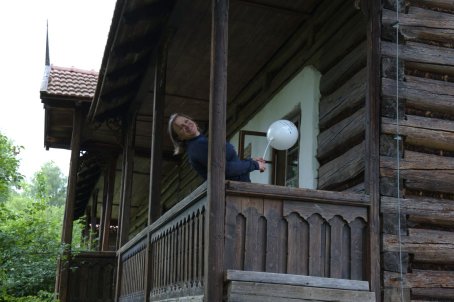 Kobieta z balonikiem przechylona za barierkę na ganku drewnianego domu