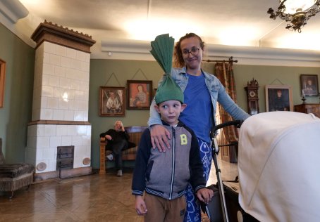 Kobieta z dzieckiem, trzyma wózek, w tle mężczyzna.