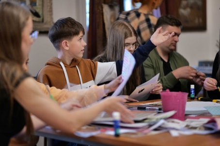 Kilka osób robi kolaże-wycinanki, na stole przybory plastyczne.