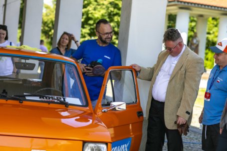 Mężczyzna otwiera drzwi do samochodu, obok ludzie