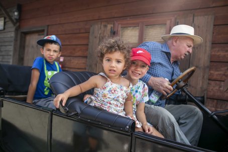 26.	Dzieci siedzą w pojeździe, mężczyzna trzyma w nim kierownicę