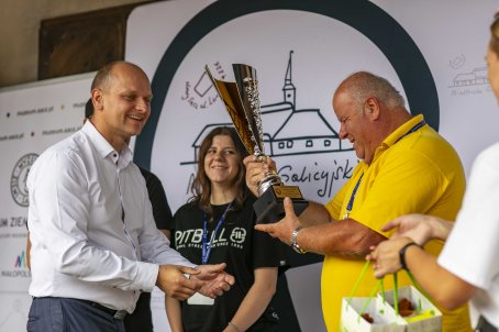 42.	Pięć osób na scenie, jeden mężczyzna trzyma puchar, osoba obok trzyma nagrody w torbach.