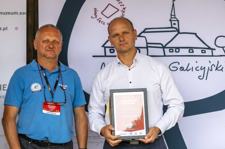 49.	Dwóch mężczyzn na scenie, jeden z nich trzyma dyplom podziękowania.