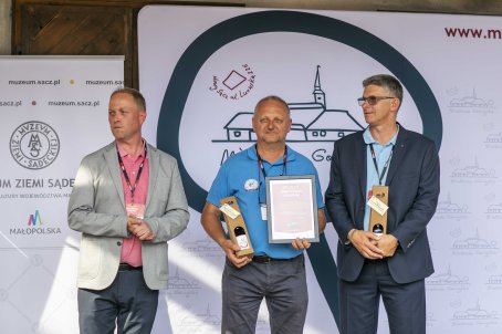 52.	Trzy osoby na scenie, mężczyźni trzymają prezenty, jeden z nich dyplom.